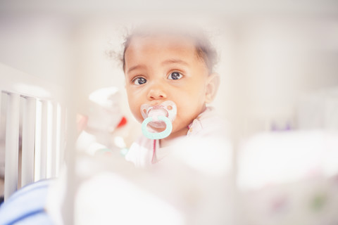 Porträt eines kleinen Mädchens mit Schnuller im Kinderbett, lizenzfreies Stockfoto