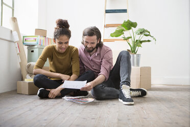 Couple sitting on floor of new flat choosing from color samples - RBF004591