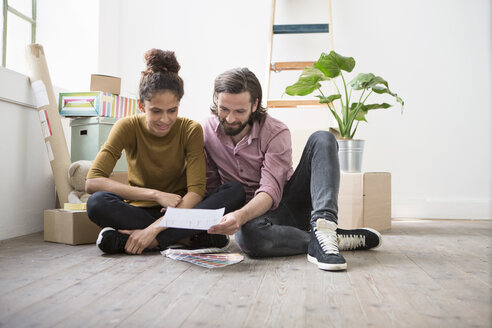 Ein Paar sitzt auf dem Boden einer neuen Wohnung und wählt aus Farbmustern aus - RBF004591