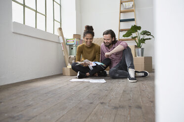 Couple sitting on floor of new flat choosing from color samples - RBF004592
