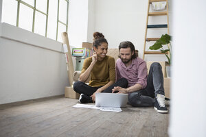 Ehepaar sitzt auf dem Boden einer neuen Wohnung und benutzt einen Laptop - RBF004593