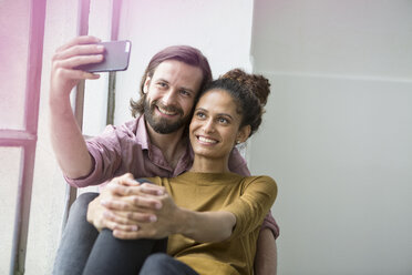 Junges Paar sitzt auf der Fensterbank und macht ein Selfie mit dem Smartphone - RBF004598