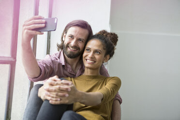 Young couple sitting on window sill taking selfie with smart phone - RBF004598