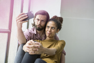 Junges Paar sitzt auf der Fensterbank und macht ein Selfie mit dem Smartphone - RBF004599