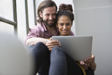 Junges Paar sitzt auf der Fensterbank und benutzt einen Laptop - RBF004603