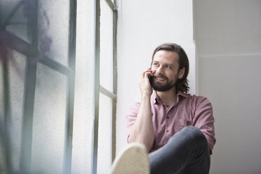 Man sitting on window sill talking on the phone - RBF004611