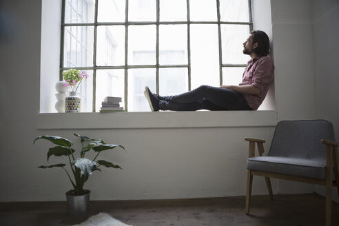 Mann sitzt auf der Fensterbank und schaut aus dem Fenster - RBF004613