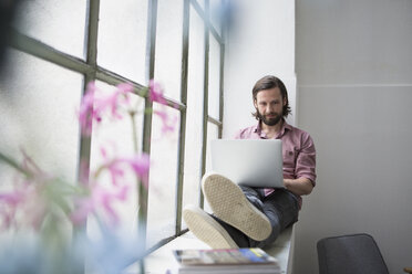 Mann sitzt auf dem Fensterbrett und benutzt einen Laptop - RBF004614