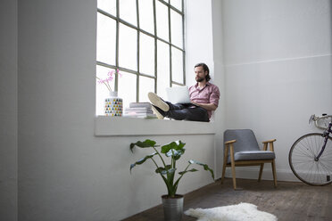 Mann sitzt auf dem Fensterbrett und benutzt einen Laptop - RBF004616