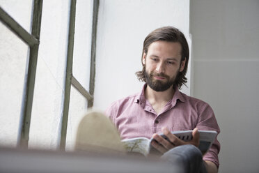 Man sitting on window sill reading magazine - RBF004620