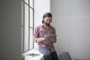 Man sitting on window sill using digital tablet - RBF004623