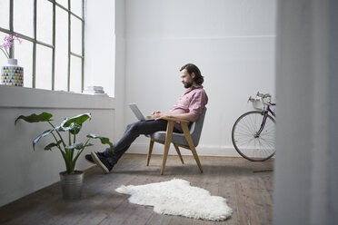 Man sitting in chair using laptop - RBF004626