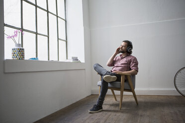 Man sitting in chair listening music with headphones - RBF004628