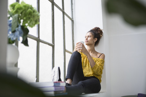 Young woman sitting on window sill with a cup of coffee stock photo