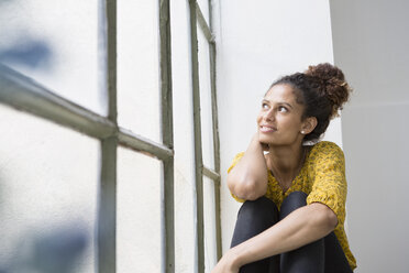 Junge Frau sitzt auf der Fensterbank und schaut aus dem Fenster - RBF004636