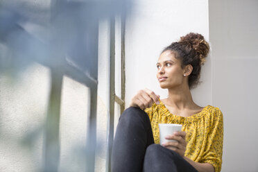 Young woman sitting on window sill with a cup of coffee - RBF004637