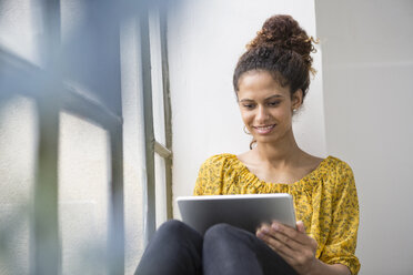 Frau auf dem Fensterbrett sitzend mit digitalem Tablet - RBF004639