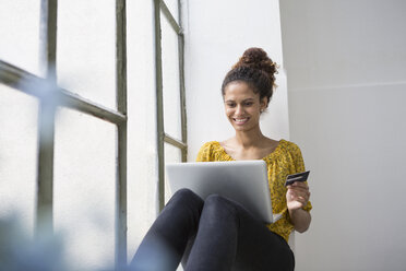 Woan sitzt mit Laptop und Kreditkarte auf der Fensterbank - RBF004641