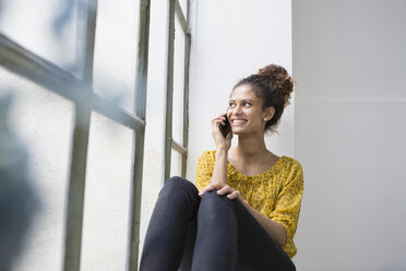 Frau sitzt auf der Fensterbank und telefoniert - RBF004642