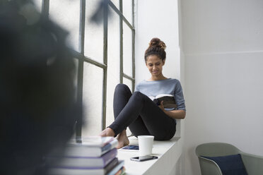 Frau sitzt auf der Fensterbank und liest ein Buch - RBF004645