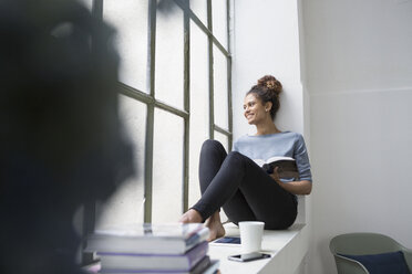 Frau sitzt auf der Fensterbank und liest ein Buch - RBF004646