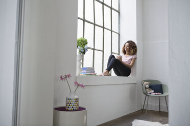 Woman sitting on window sill drinking cup of coffee - RBF004651