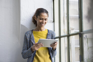 Young woman standing at the window using digital tablet - RBF004665