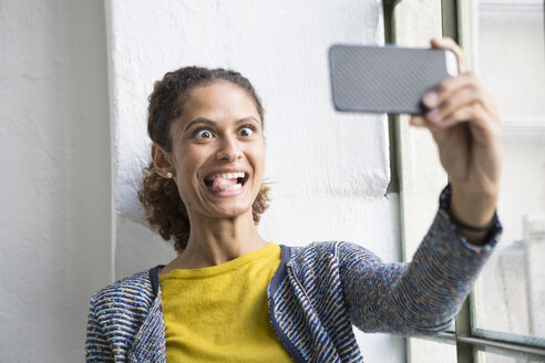 Junge Frau steht am Fenster und macht ein Selfie mit ihrem Smartphone - RBF004667