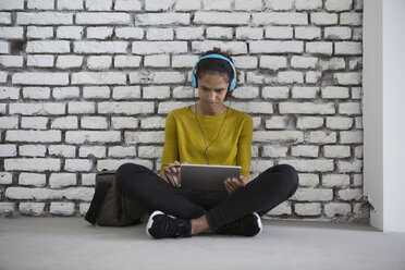 Junge Frau mit Kopfhörern sitzt auf dem Boden und benutzt ein digitales Tablet - RBF004668