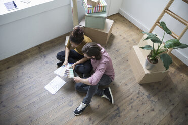 Couple sitting on floor of new flat choosing from color samples - RBF004672