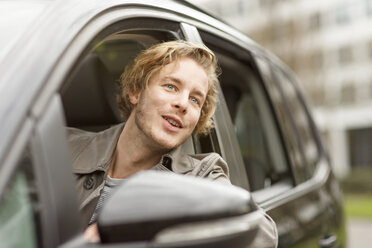 Portrait of smiling young man leaning out of car window watching something - PESF000192