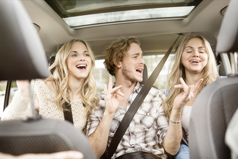 Drei Freunde sitzen auf der Rückbank eines Autos und singen zusammen, lizenzfreies Stockfoto