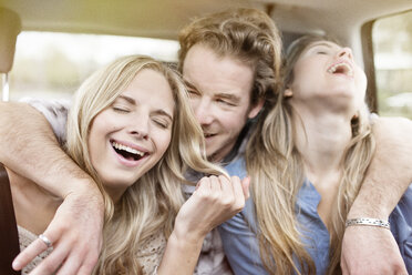 Drei lachende Freunde sitzen auf der Rückbank eines Autos und haben Spaß - PESF000195