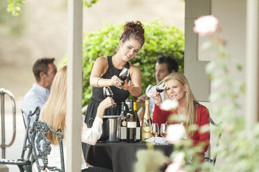 Kellnerin und Kunden in einem Restaurant, die Wein in Gläsern prüfen - ZEF008903