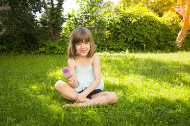 Portrait of happy little girl sitting on a meadow with blueberry ice lolly - LVF005085