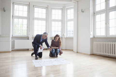 Immobilienmakler zeigt einem Kunden in einer leeren Wohnung einen Bauplan, lizenzfreies Stockfoto