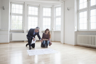 Immobilienmakler zeigt einem Kunden in einer leeren Wohnung einen Bauplan - RBF004680