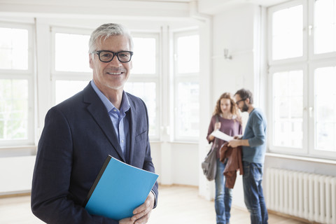 Porträt eines lächelnden Immobilienmaklers mit einem Paar im Hintergrund, lizenzfreies Stockfoto