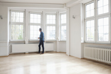 Man looking out of window in empty apartment - RBF004689