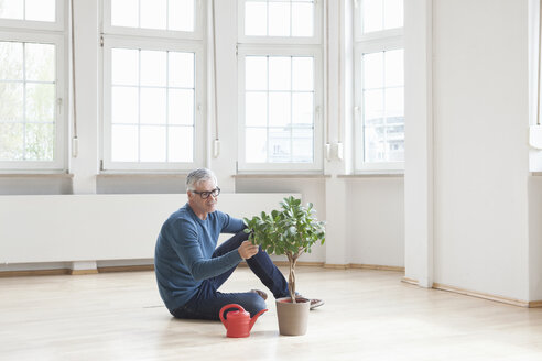 Man sitting on floor with plant in empty apartment - RBF004691