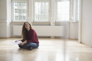 Woman sitting on floor in empty apartment looking around - RBF004719