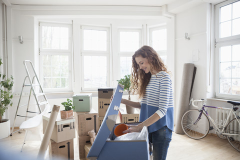 Frau in neuer Wohnung beim Auspacken eines Kartons, lizenzfreies Stockfoto