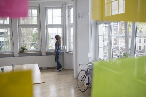 Frau im Büro schaut aus dem Fenster - RBF004738