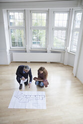 Real estate agent showing construction plan to client in empty apartment - RBF004743