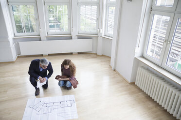 Real estate agent showing construction plan to client in empty apartment - RBF004744