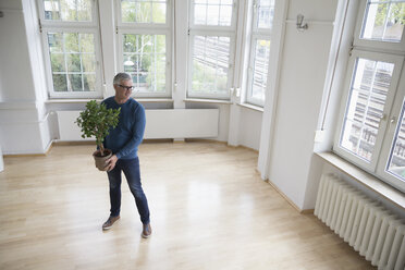 Man holding plant in empty apartment - RBF004748