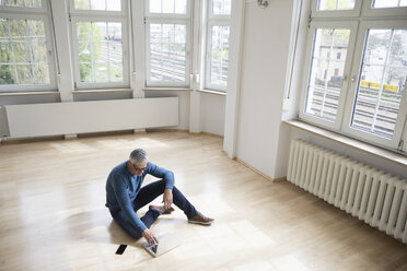 Man using laptop in empty apartment - RBF004751