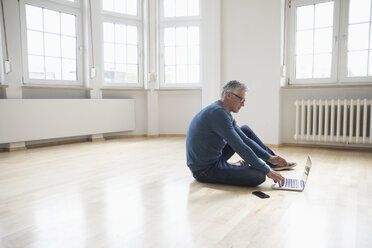 Man using laptop in empty apartment - RBF004752