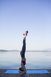 Young woman doing exercise on pier, headstand - MRAF000098