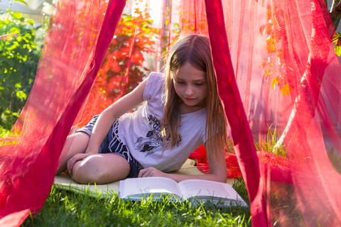Girl sitting on a meadow under mosquito net reading a book stock photo